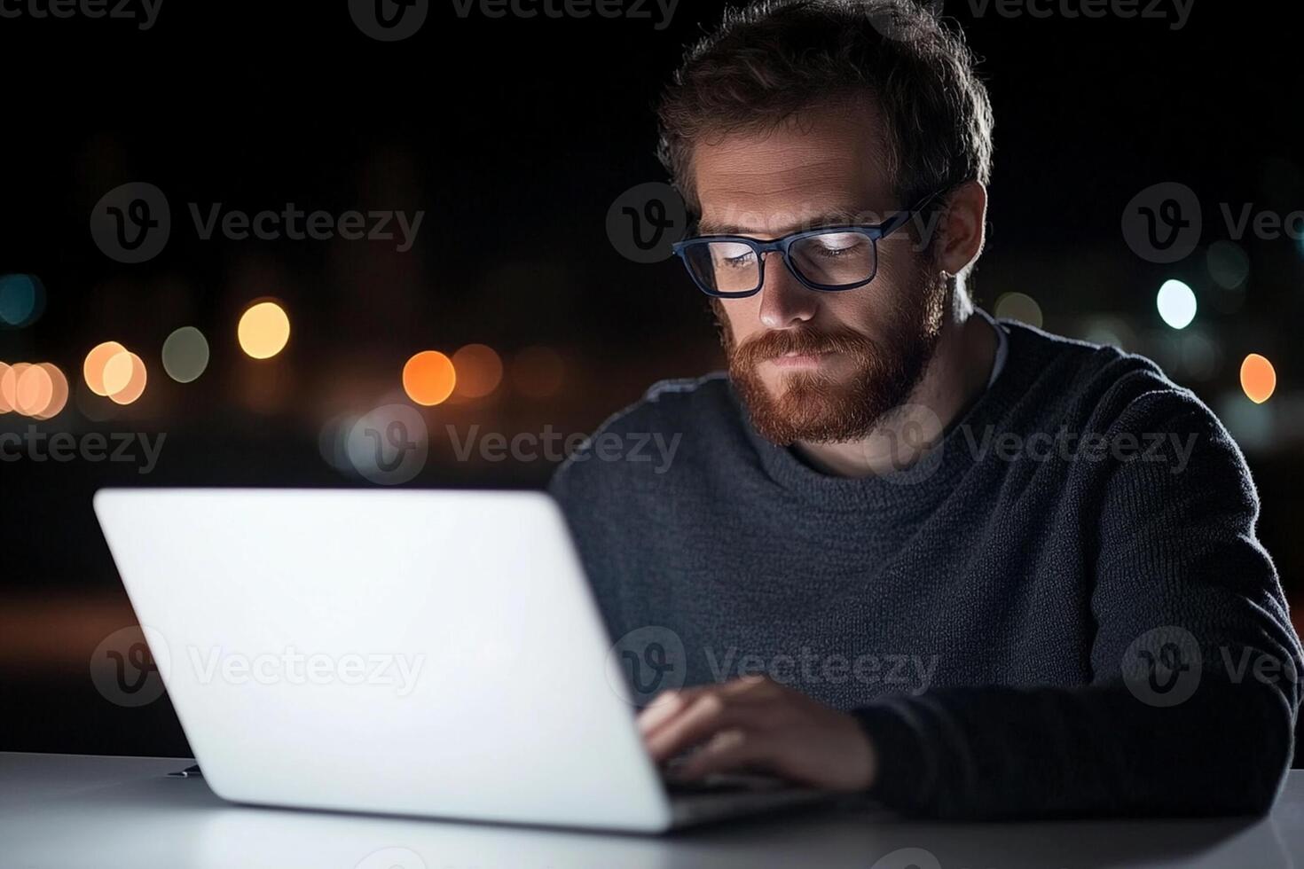 A man with glasses and a beard is working on his laptop at night photo
