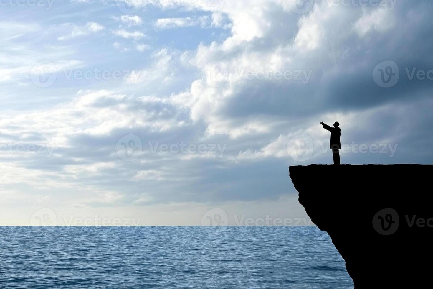 A man standing on the edge of a cliff looking out over the ocean photo