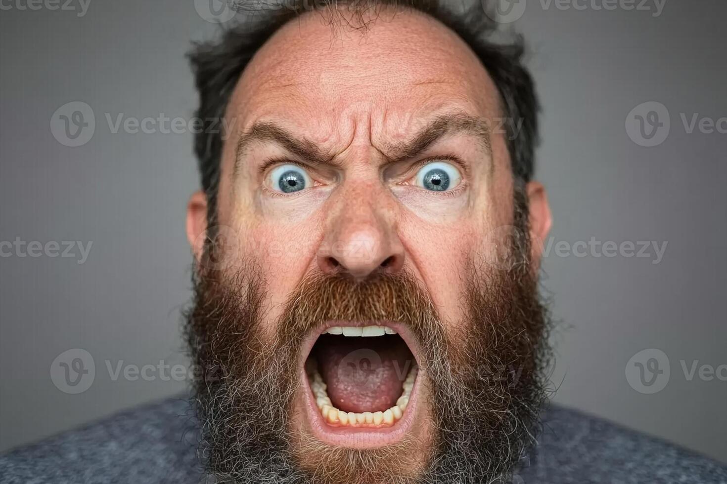 A man with a beard and a blue shirt is making an angry face photo