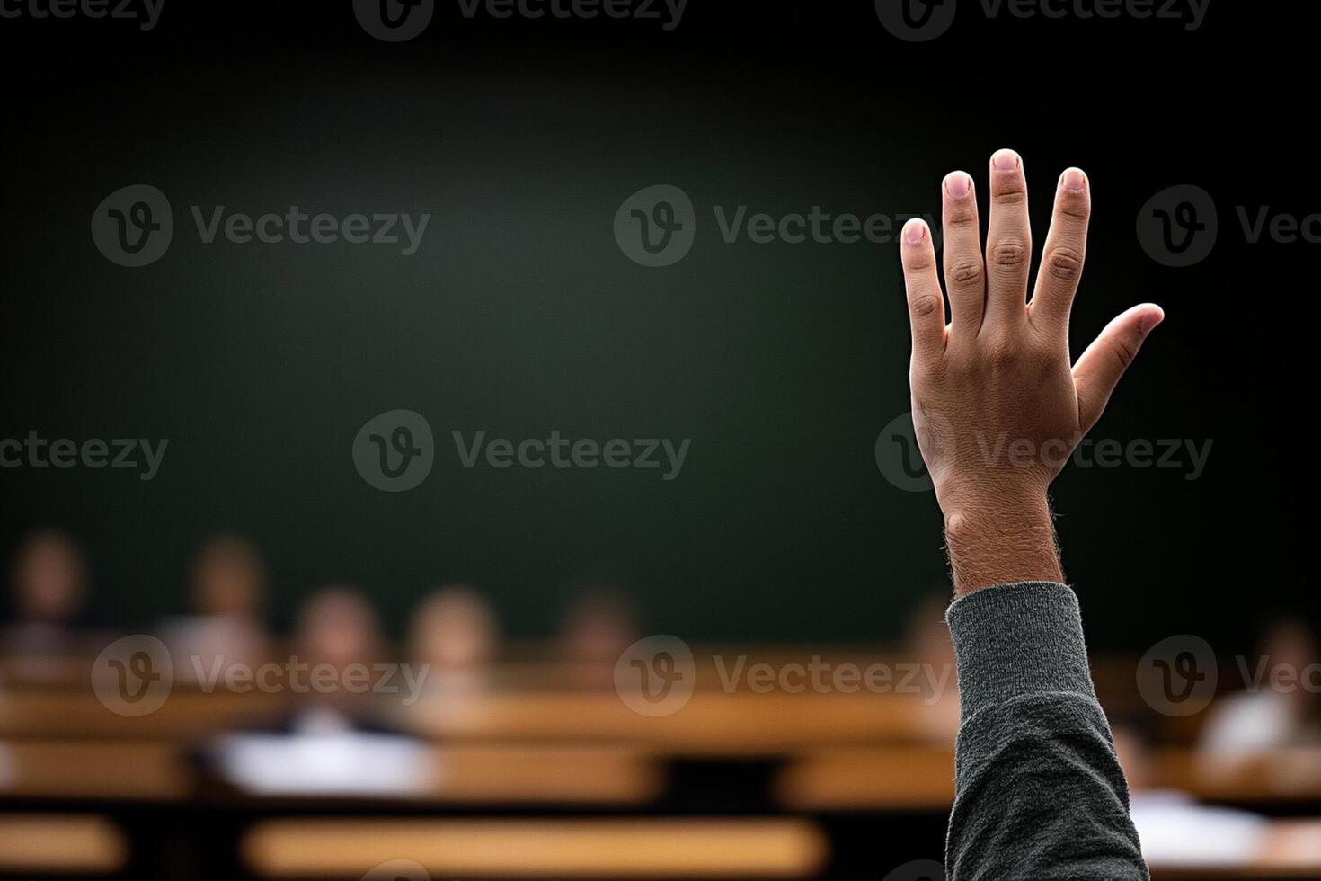 A hand raised in front of a classroom photo