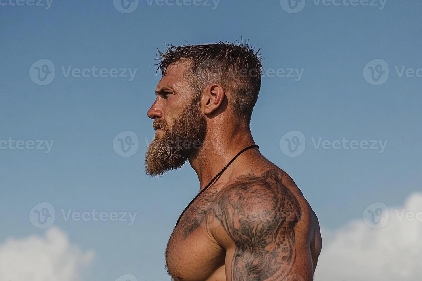 A man with a beard and tattoos standing on the beach photo