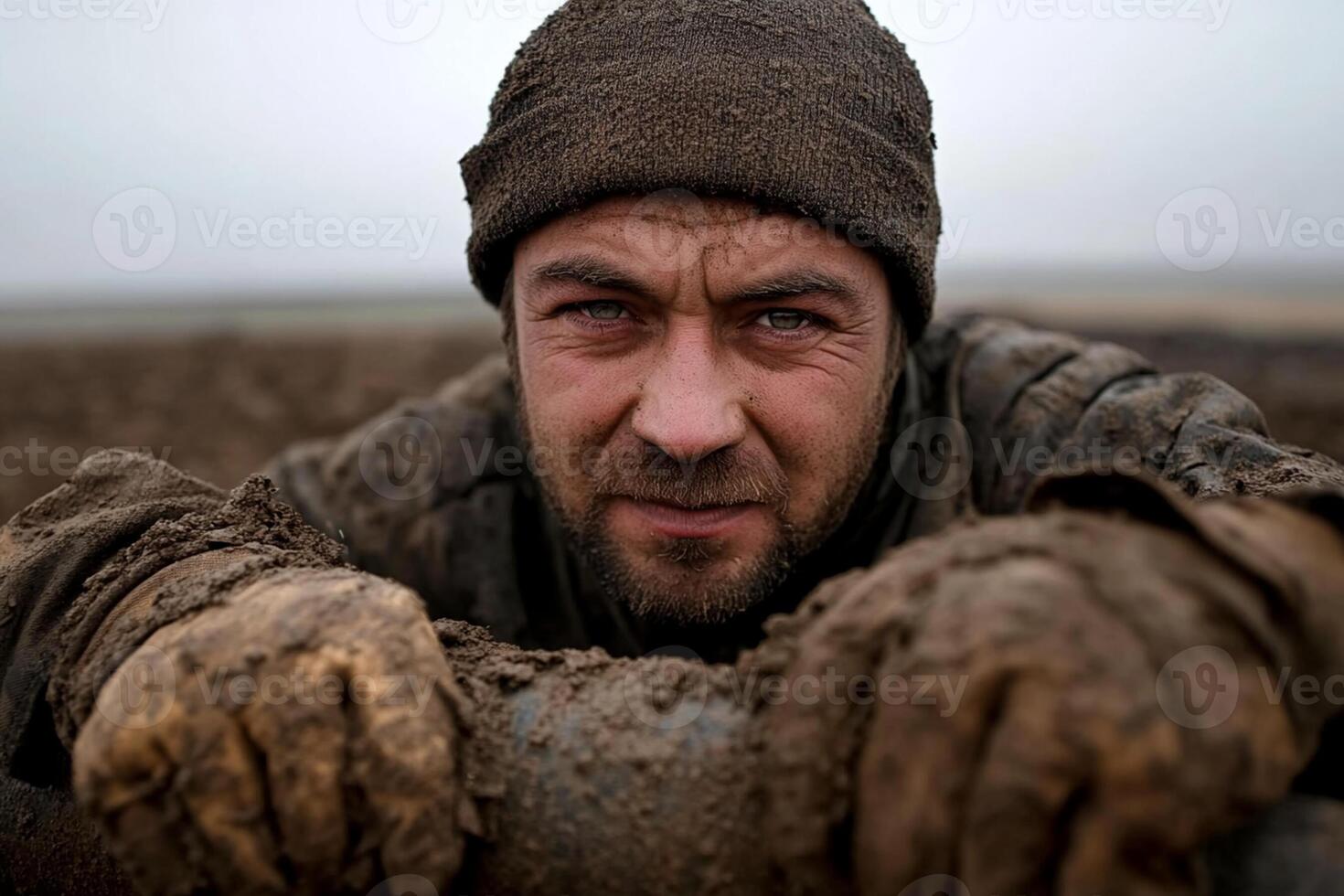 A man in a muddy field with his hands on the pipe photo