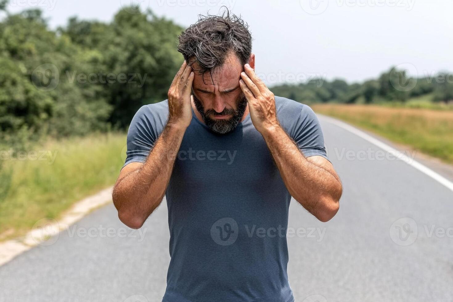 A man is holding his head in pain while standing on a road photo
