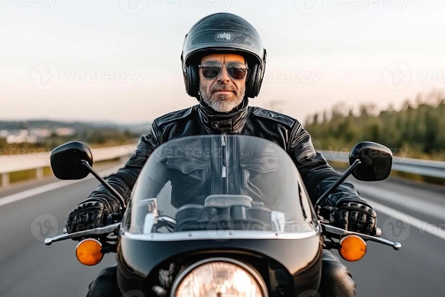 A man wearing a leather jacket and sunglasses rides a motorcycle photo