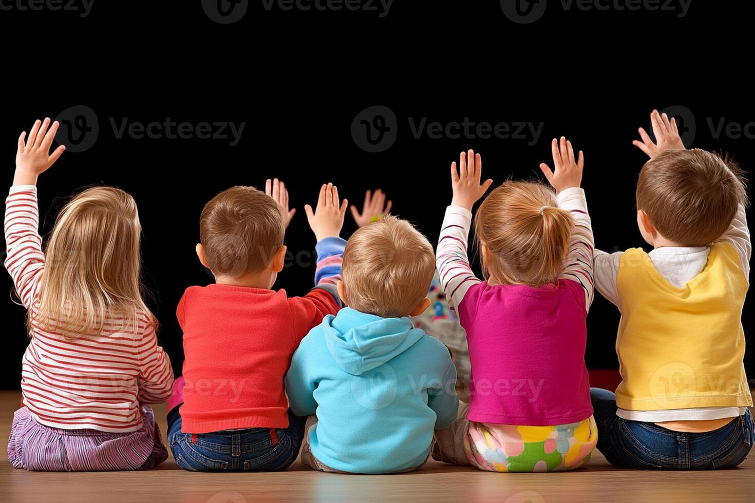 A group of children sitting on the floor with their hands up photo