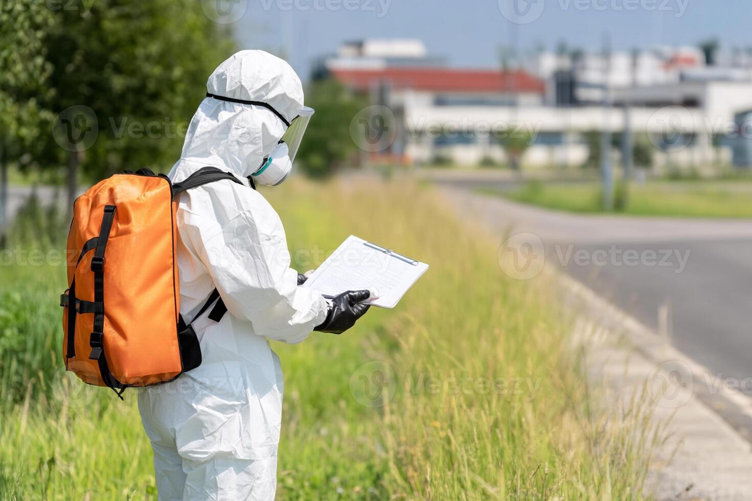 A person in a protective suit and mask is standing on the side of the road photo