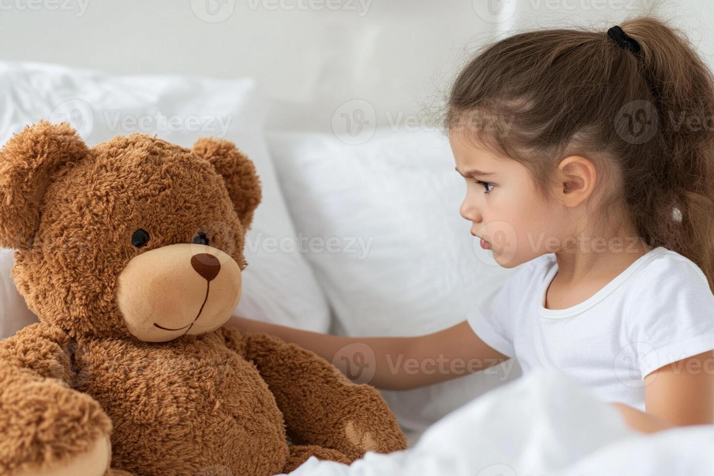 A little girl is sitting on a bed with a teddy bear photo