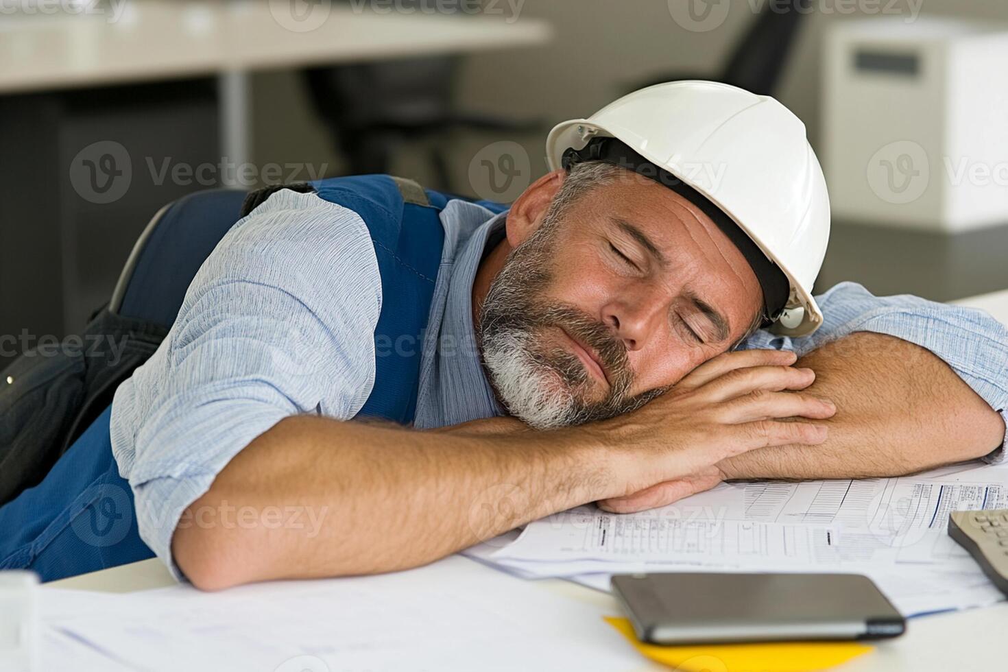 A man sleeping on a desk with a hard hat photo