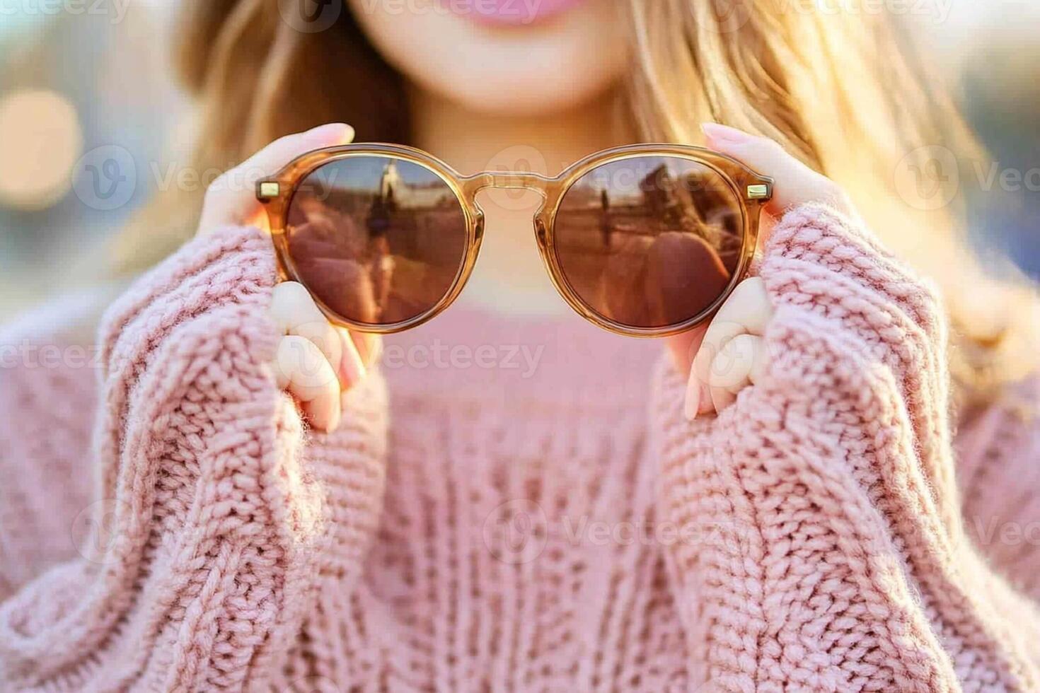 A woman in a pink sweater holding up her sunglasses photo