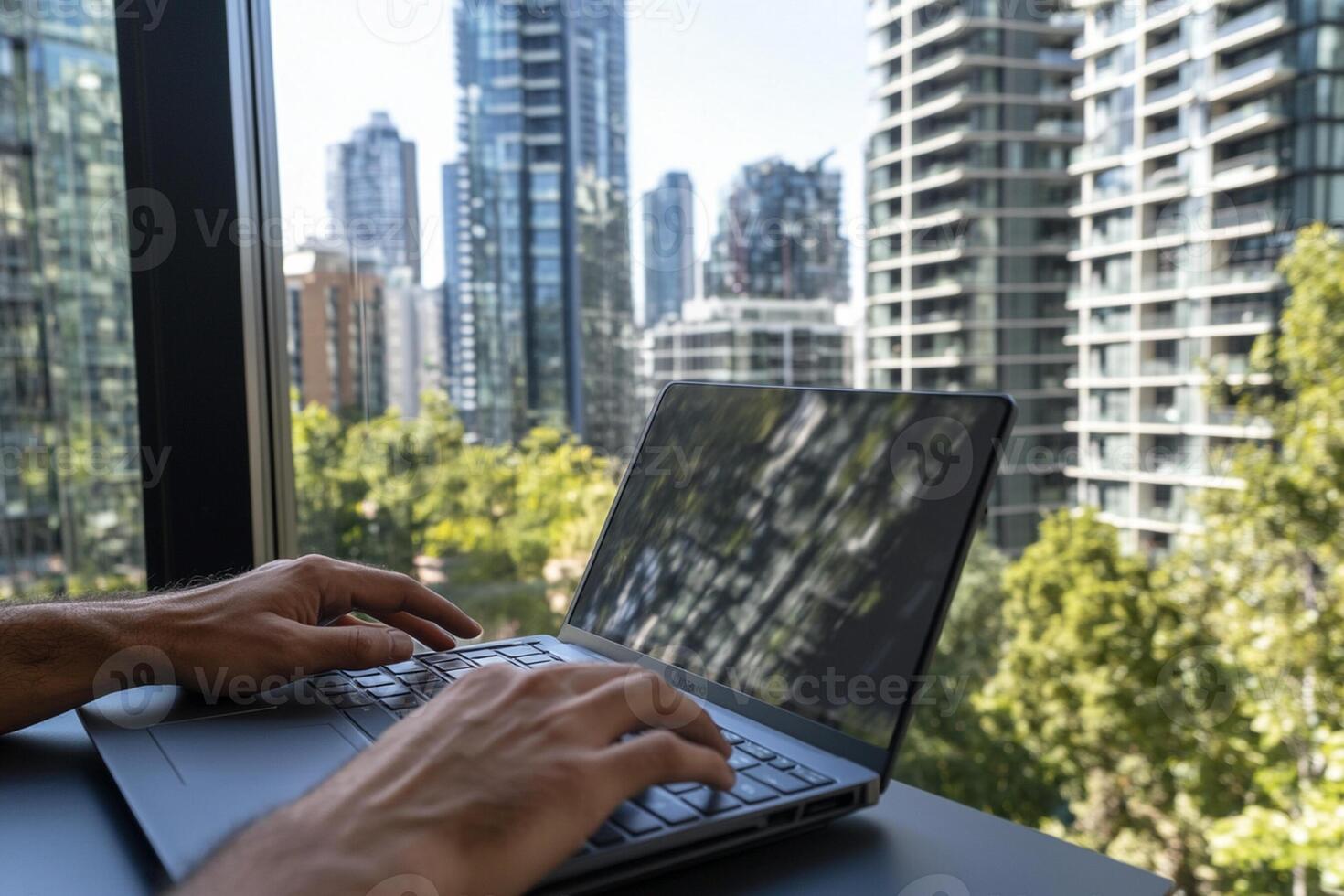 A person typing on a laptop in front of a window photo