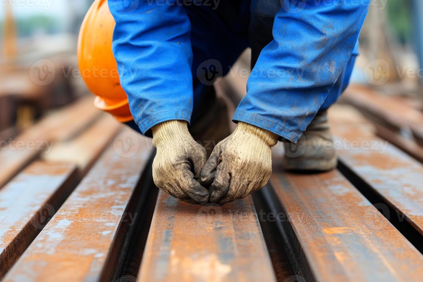A man in blue overalls and gloves is working on a wooden plank photo