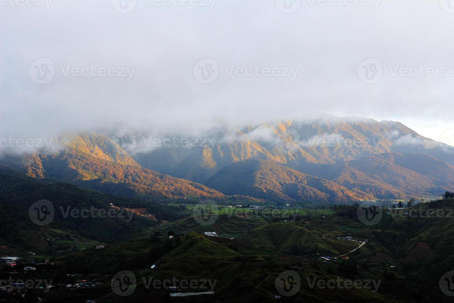 A breathtaking view of misty green mountains, rural villages, and lush valleys under a dramatic cloudy sky, creating a serene natural scene photo