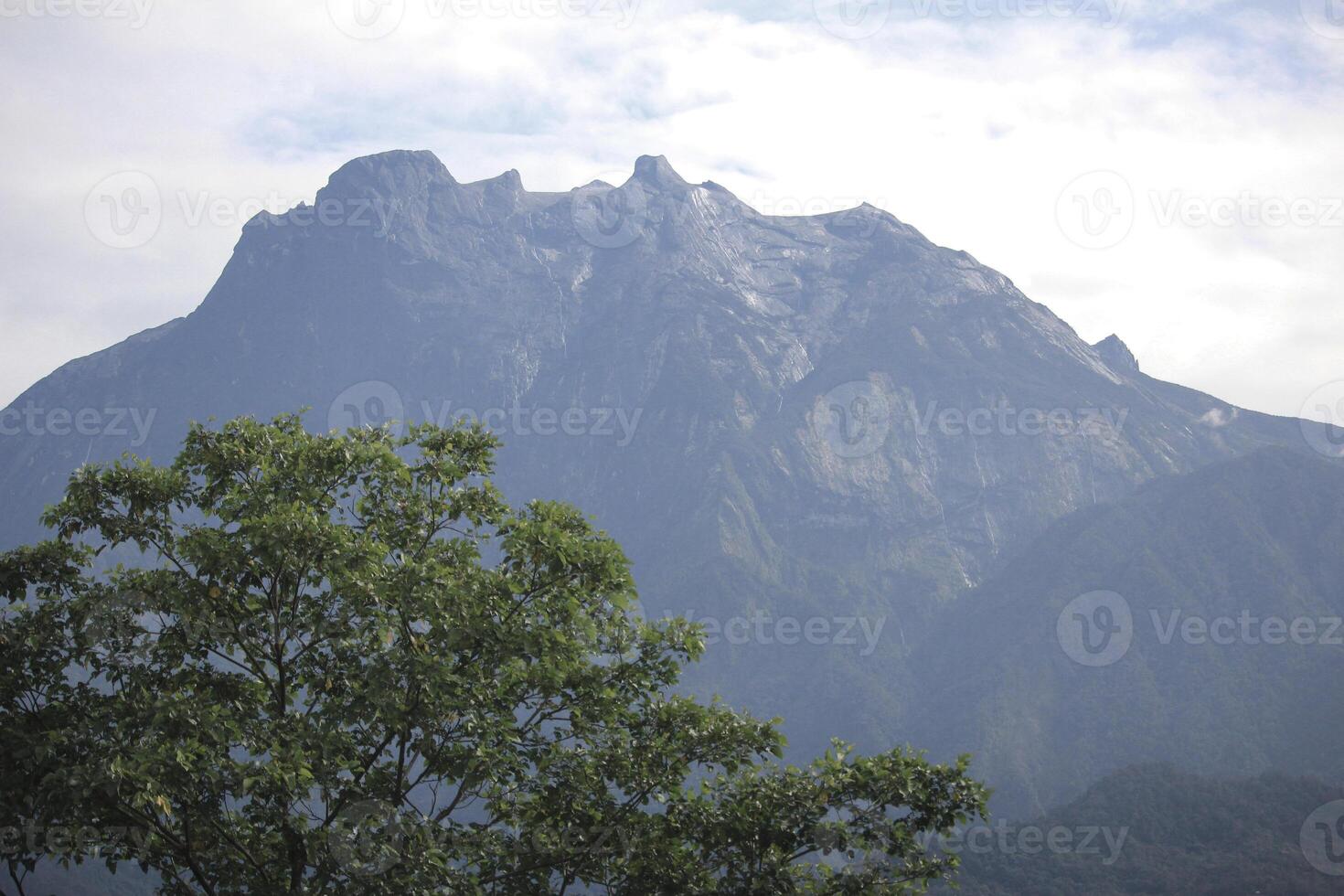 Majestic Mount Kinabalu Peak with Lush Greenery Under Cloudy Sky in Borneo photo