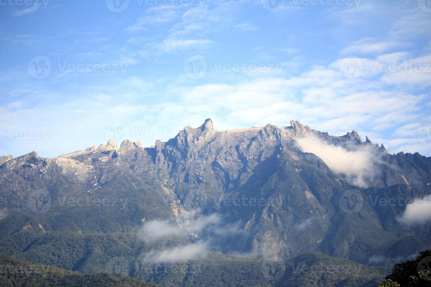 A breathtaking mountain peak with rugged rocky formations, partially covered by mist, under a cloudy sky photo