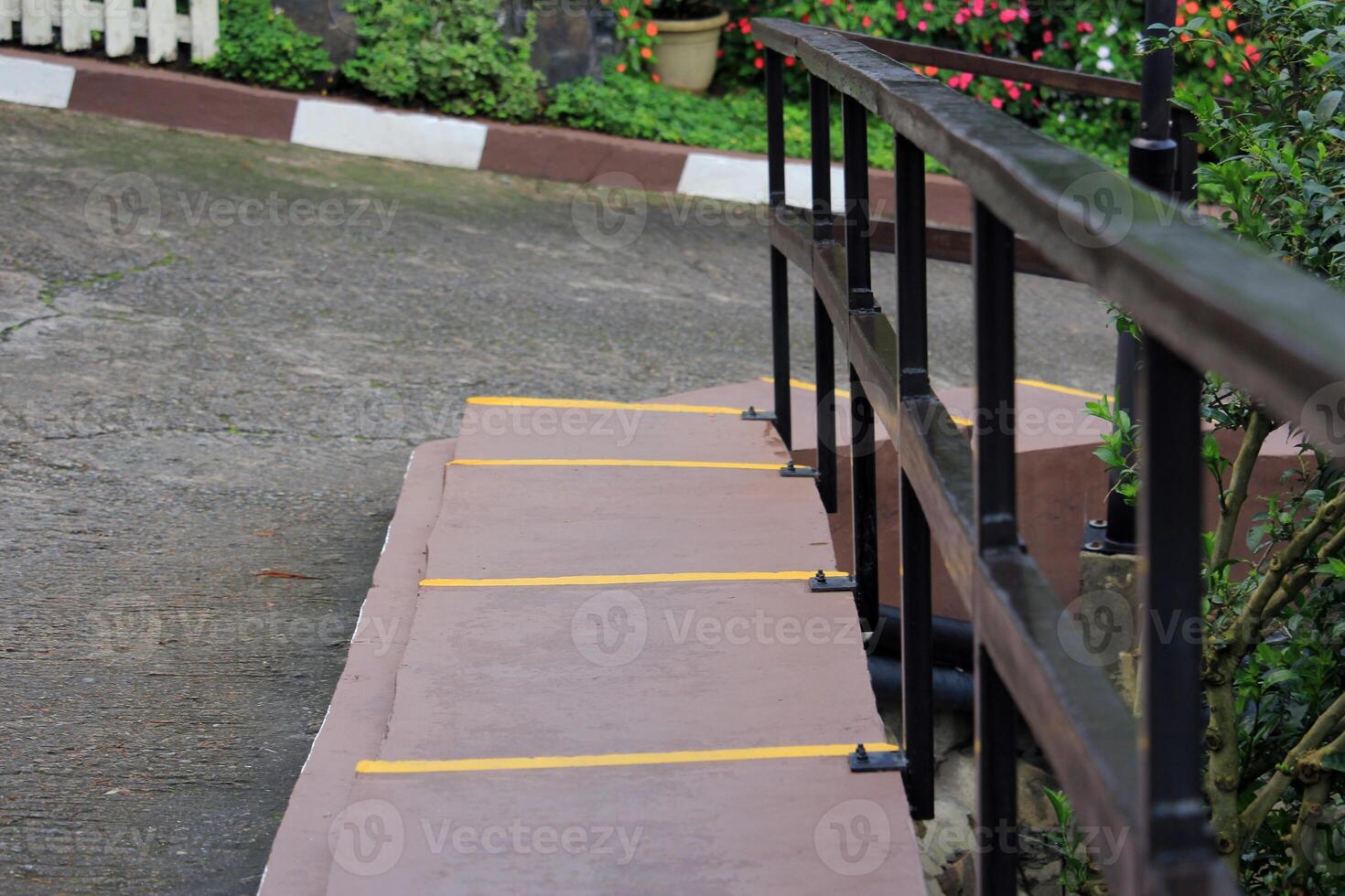 Concrete stairs with black metal handrails, highlighted with yellow safety lines, surrounded by lush greenery and colorful flowers in an outdoor setting photo