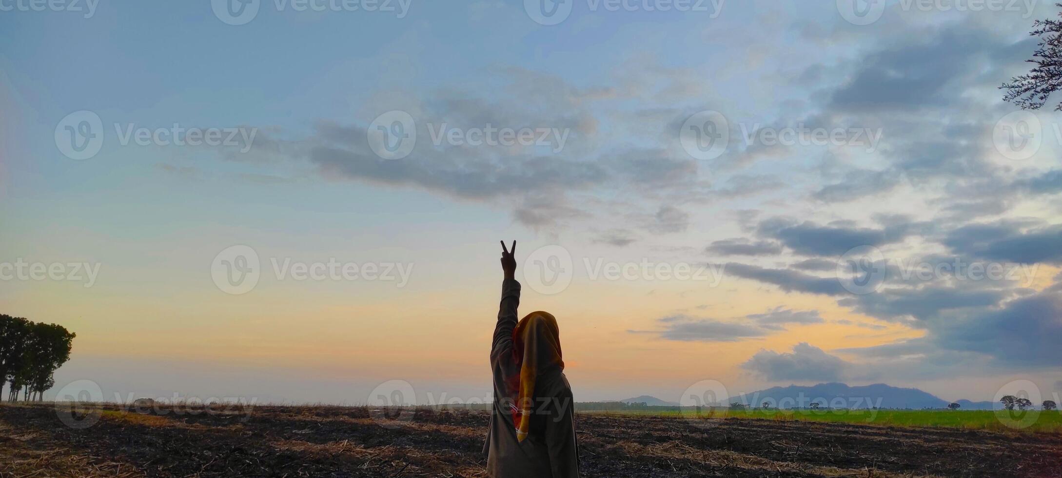 Woman in a hijab making a v shape with her hands against the setting sun. photo
