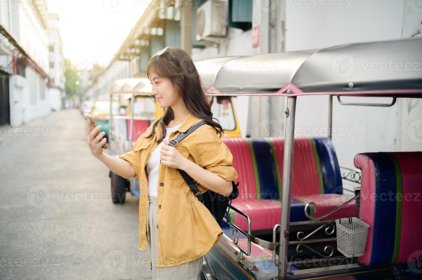 Asian woman using smartphone while standing next to tuk tuk photo