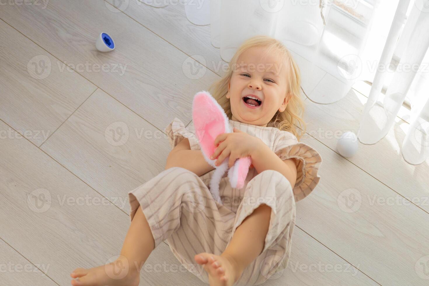 Child lying on floor with bunny ears and colorful eggs during a playful holiday celebration photo