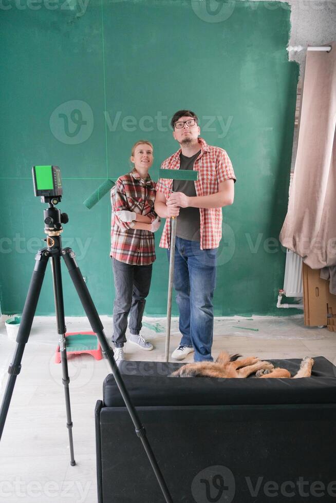 Happy couple renovating new house apartment measuring wall with laser level photo