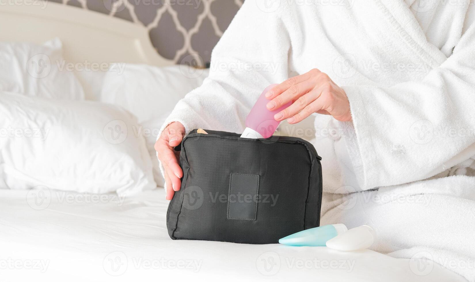 woman hands holding cosmetic travel kit bed. colorful cosmetic bottles photo