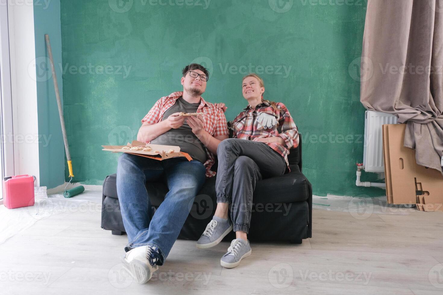 couple renovating new house apartment , sitting on the couch and eating pizza, discussing plans together and petting a cute dog photo