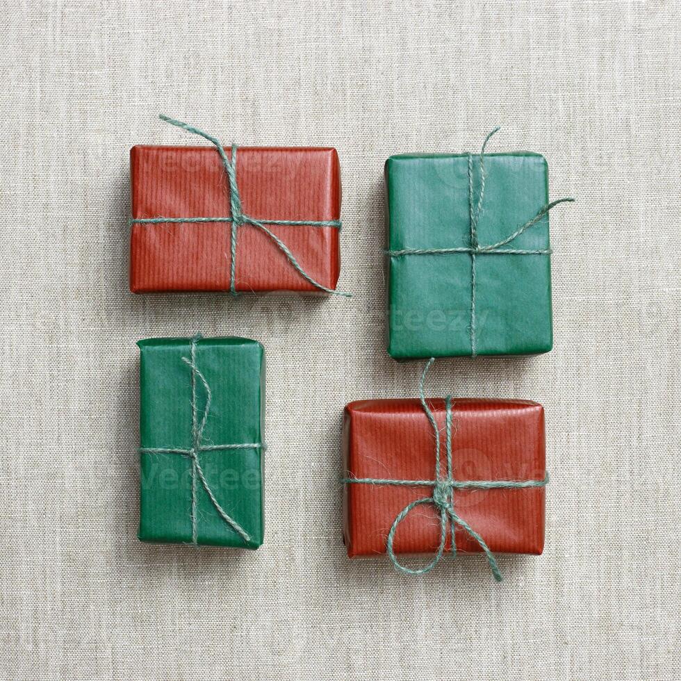 Holiday handmade gift boxes, square geometric pattern on linen cloth background, green, red paper-wrapped presents with rough thread, minimal aesthetic flat lay gifts simple present handmade photo
