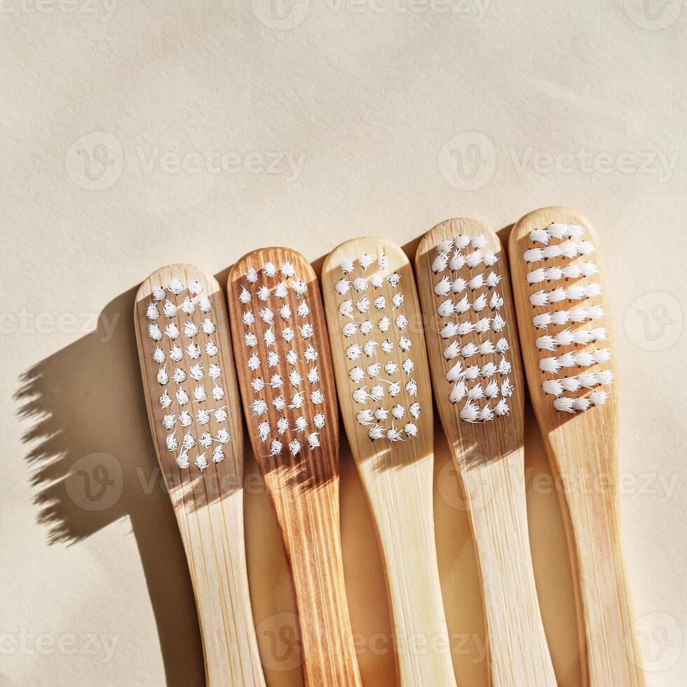 Eco friendly Bamboo toothbrushes with white bristles at sunlight with dark shadows on beige background. Sustainable living concepts, minimal style aesthetic photo, top view set wooden brushes photo