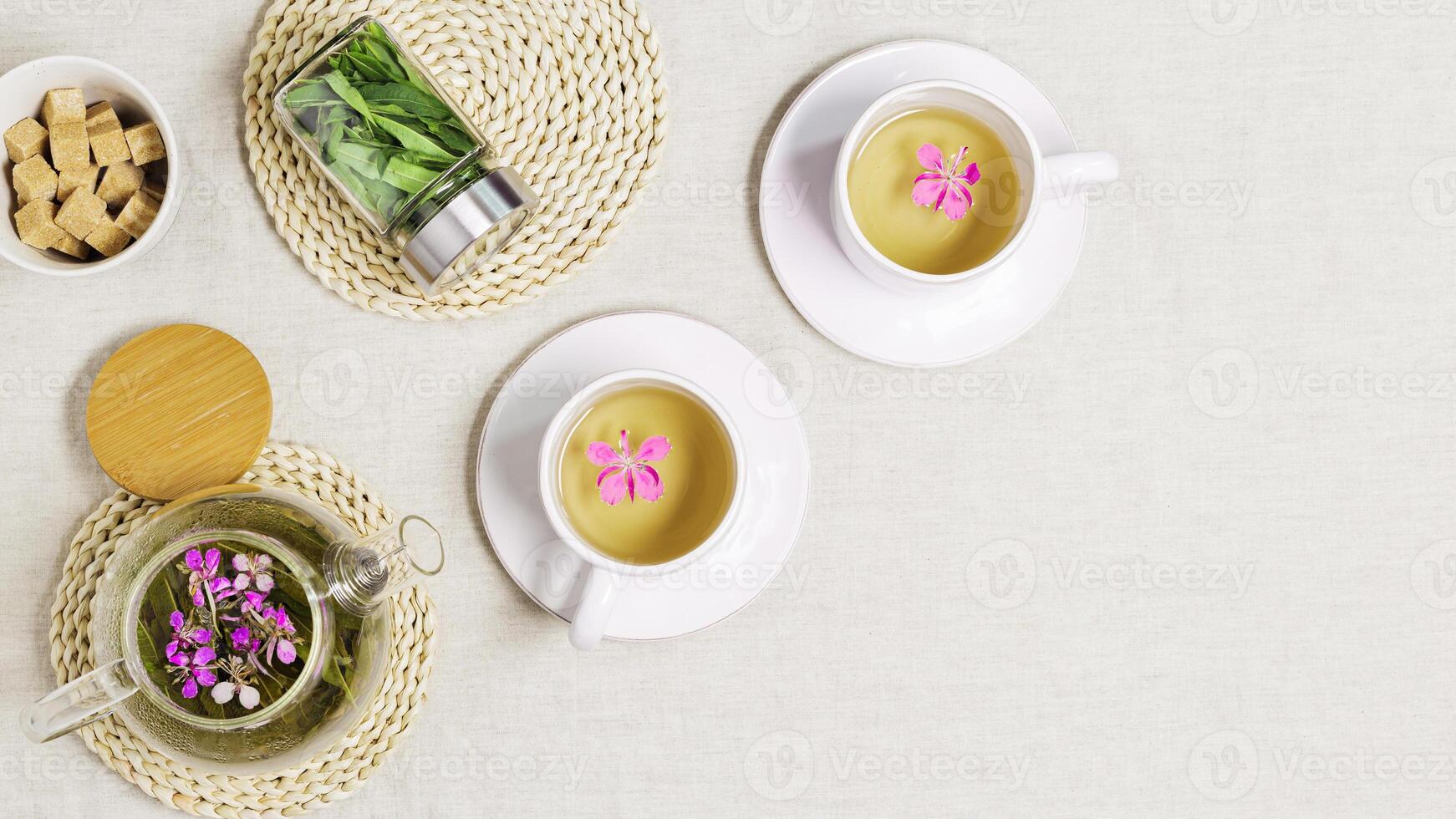 Fireweed tea in white cup and transparent glass teapot, herbal hot tea from green leaves of ivan chai on textile tablecloth. Top view healthy drink and wild flowering willow herb, tea time photo