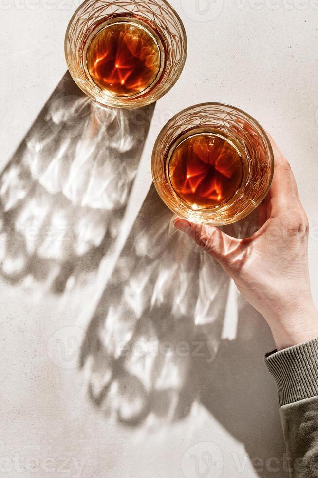 Transparent alcohol Glasses with dark shadows at sunlight on beige table, hand holding glass with alcohol, top view minimal style, aesthetic flat lay shiny glass at natural light, summer drink photo