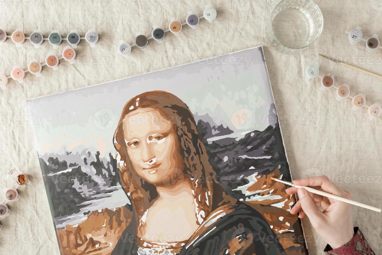 Painting by numbers with acrylic paints. Woman coloring Mona Lisa picture by numbers, hand with brush and paints of different colors. Creative hobby for relaxation, leisure activity at home photo