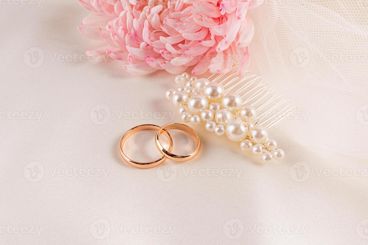 Two gold wedding rings, a pearl hairpin, a delicate champagne veil against a background of beige satin with a flowers. beautiful layout, invitation. photo