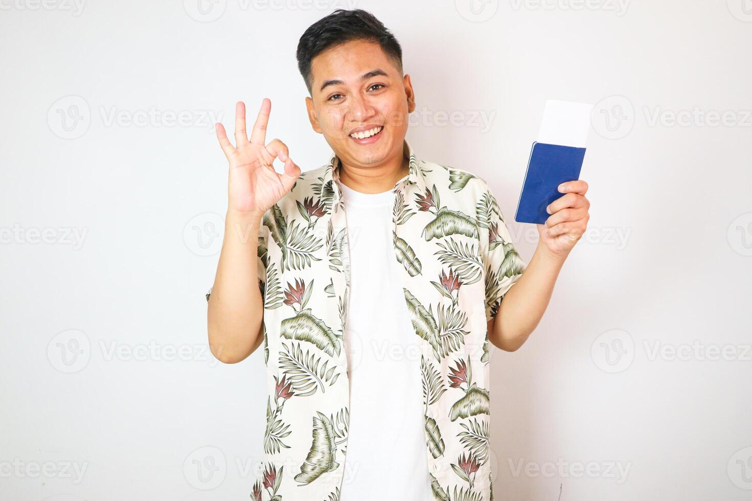A happy asian guy shows his newly acquired Indonesian Passpor with ok sign, Isolated on a white background. photo