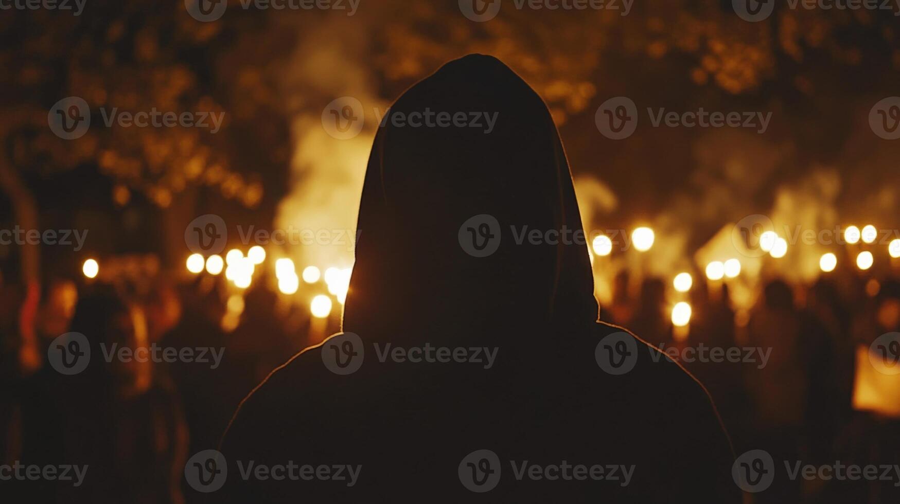 Hooded protestor witnessing night demonstration with torches and smoke photo