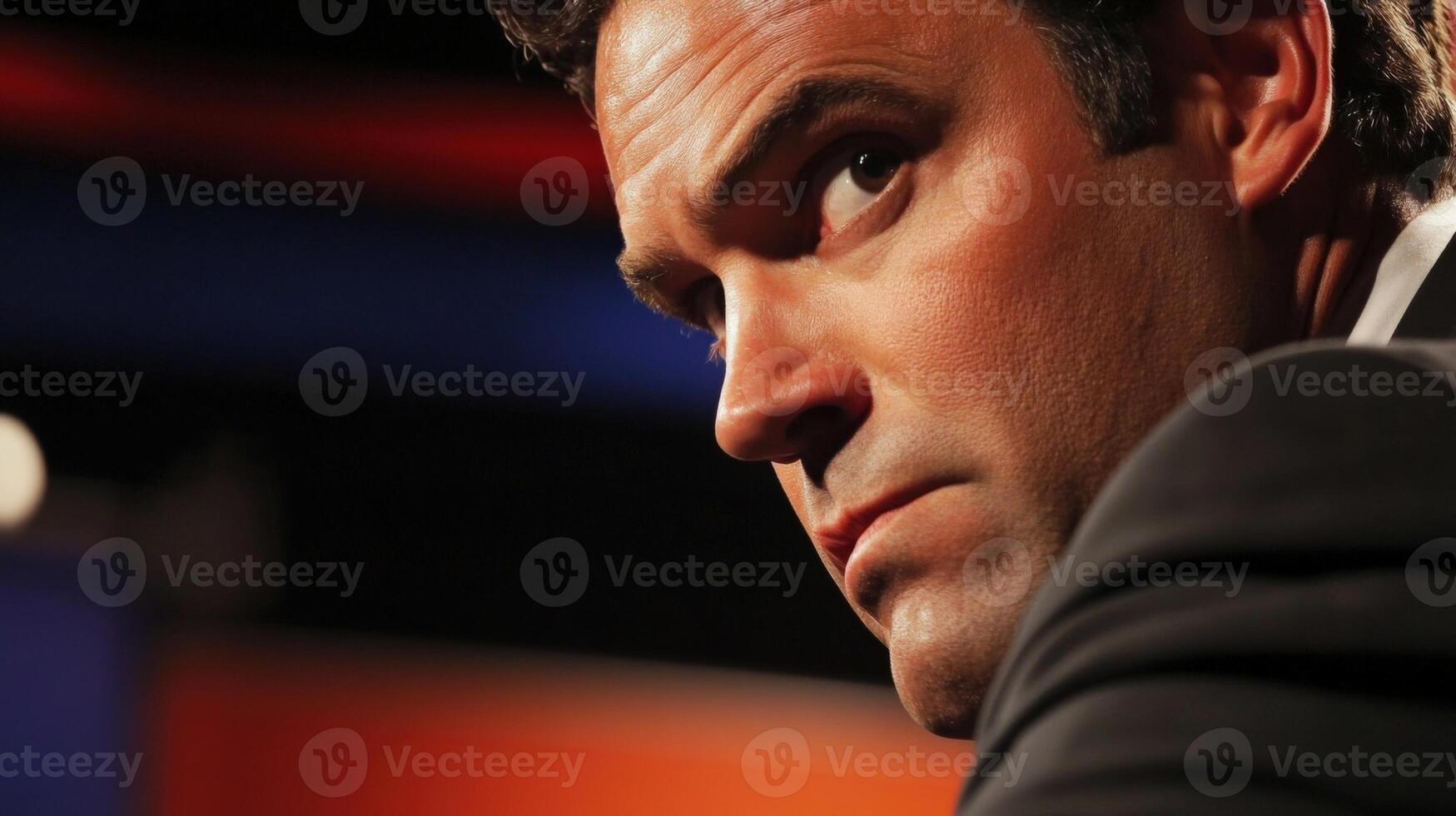 A politician leans slightly forward intensely engaged in a heated discussion with furrowed brows and a determined expression. The closeup reveals the details of their suit and tie photo