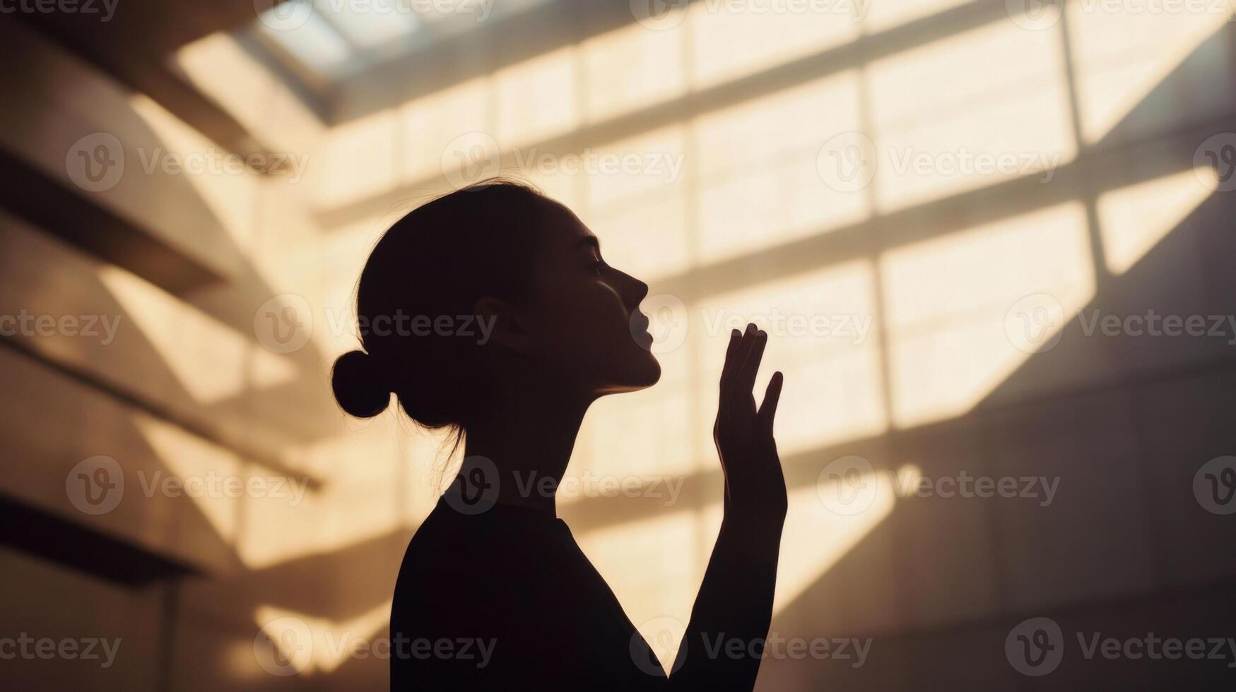 A midaged figure silhouetted against a softly blurred backdrop of angular modern structures raises an open palm to their face signifying deep reflectio photo