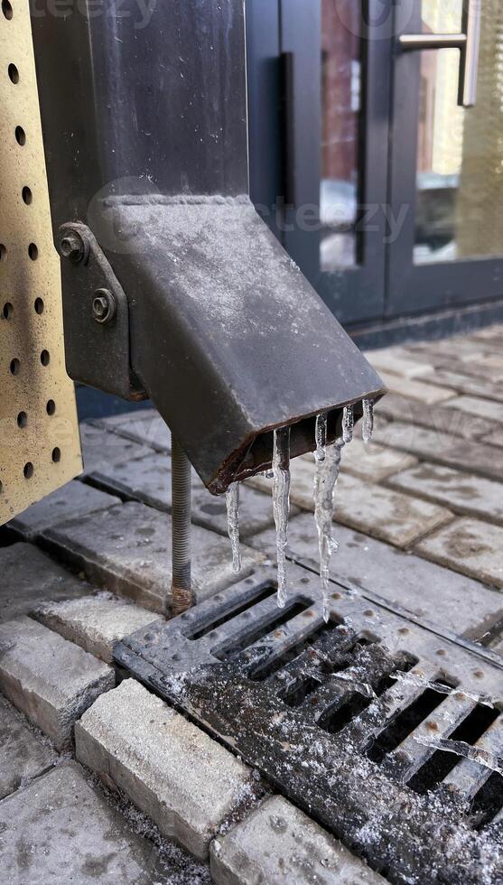 Icy scene of frozen icicles hanging from drainpipe. The image captures cold weather effects and seasonal change on metal pipe, with ice forming near ground photo