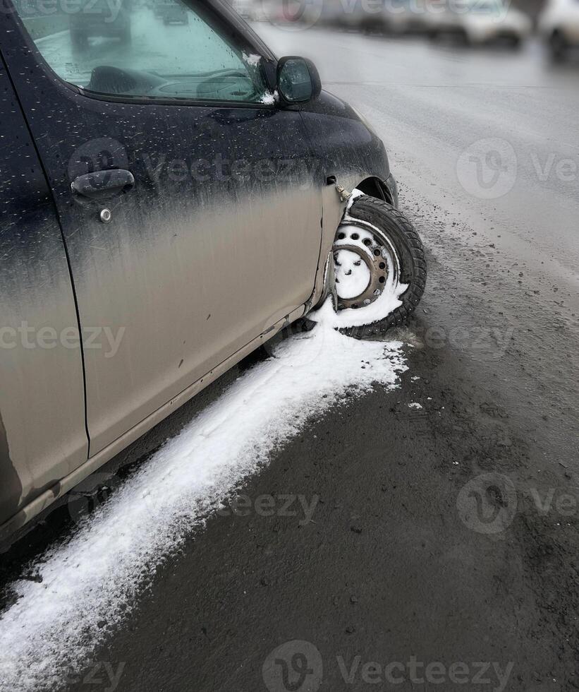 Close-up image of a car with a detached front wheel, stuck in snowy and icy road conditions. Visible damage to the vehicle emphasizes road safety challenges during winter photo