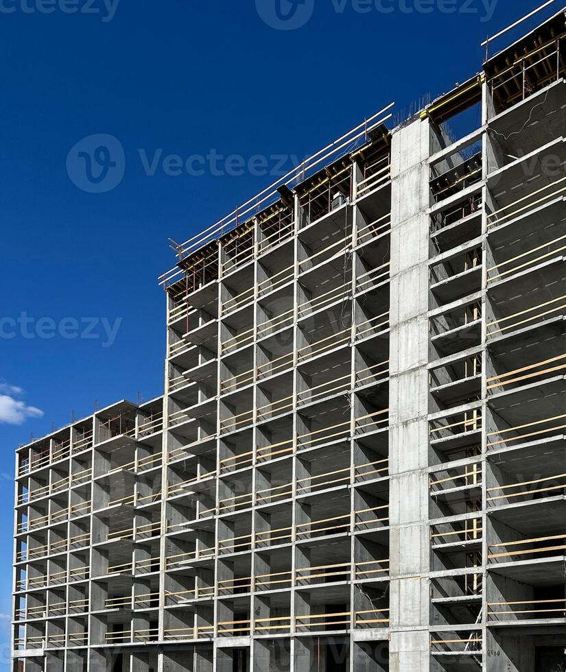 High-rise building under construction with exposed concrete framework and wooden scaffolding under a clear blue sky background, modern urban development progress photo