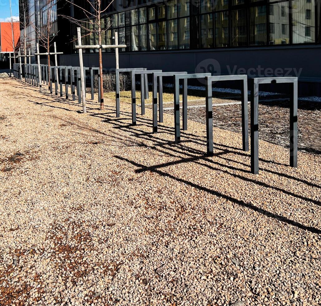 Empty metal bike racks lined up on gravel path outside a modern building, casting distinct shadows on the ground in quiet urban setting copy space photo