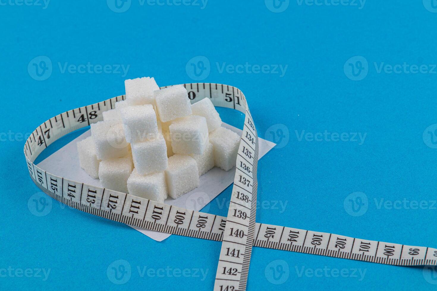 Sugar cubes arranged in heart shape with measuring tape on blue background photo