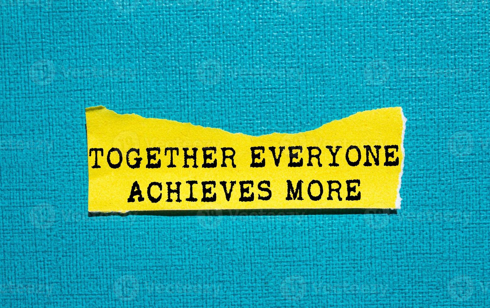 Together everyone achieves more message written on ripped torn yellow paper piece on blue background. Conceptual together everyone achieves more symbol. Copy space. photo