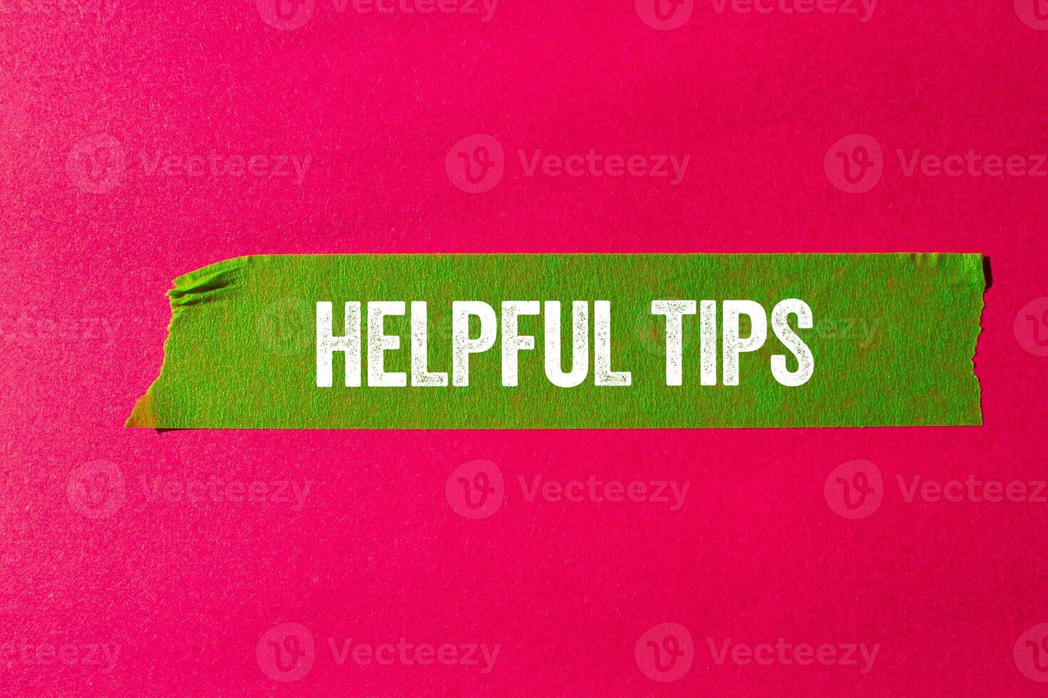 Helpful tips message written on ripped torn green paper tape on pink background. Conceptual helpful tips symbol. Copy space. photo