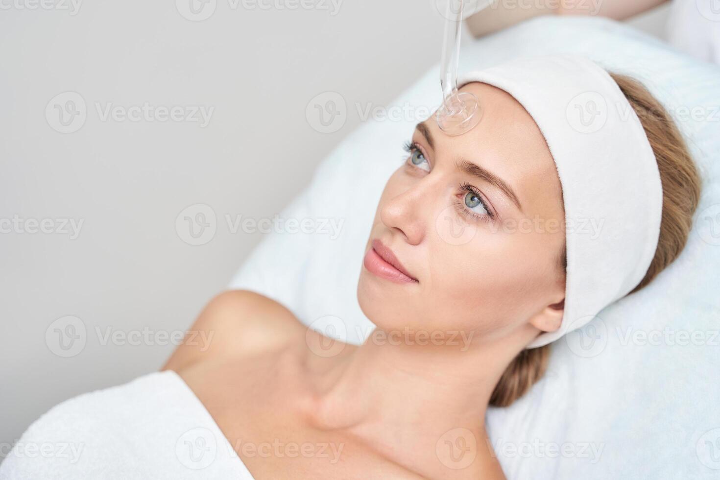 Caucasian female receiving facial spa treatment with skincare product application in wellness center. photo