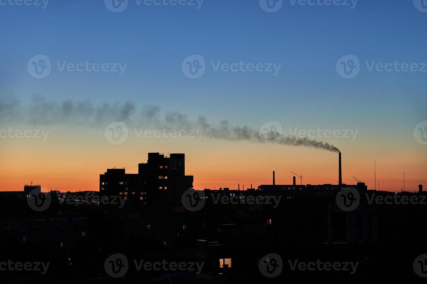 City skyline and factory at sunset with smoke plume against colorful evening sky. photo
