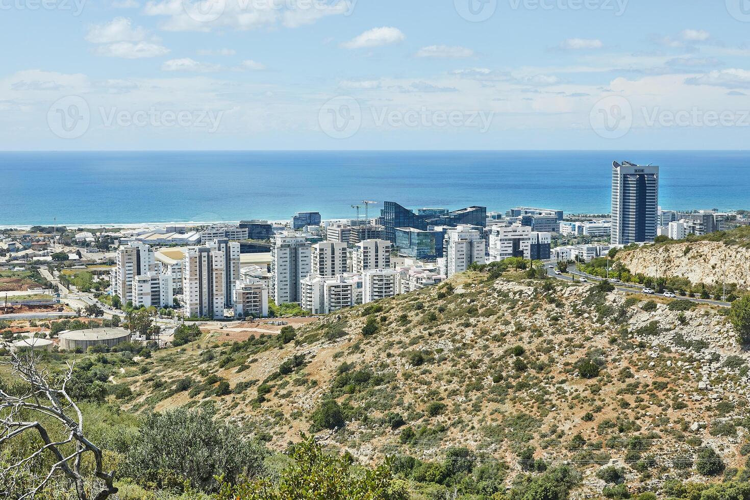 A modern coastal city with tall buildings meets the serene blue sea under a bright sky, showcasing urban life and nature photo