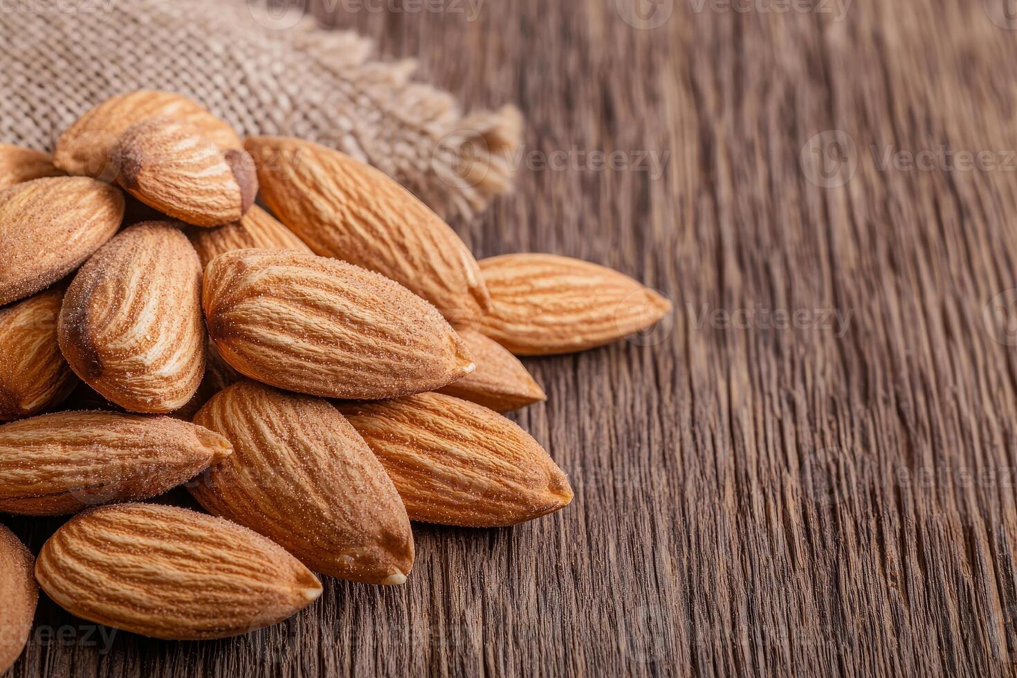 A close-up of raw almonds scattered on a wooden surface, showcasing their natural texture and color, with a burlap sack partially visible in the background. photo