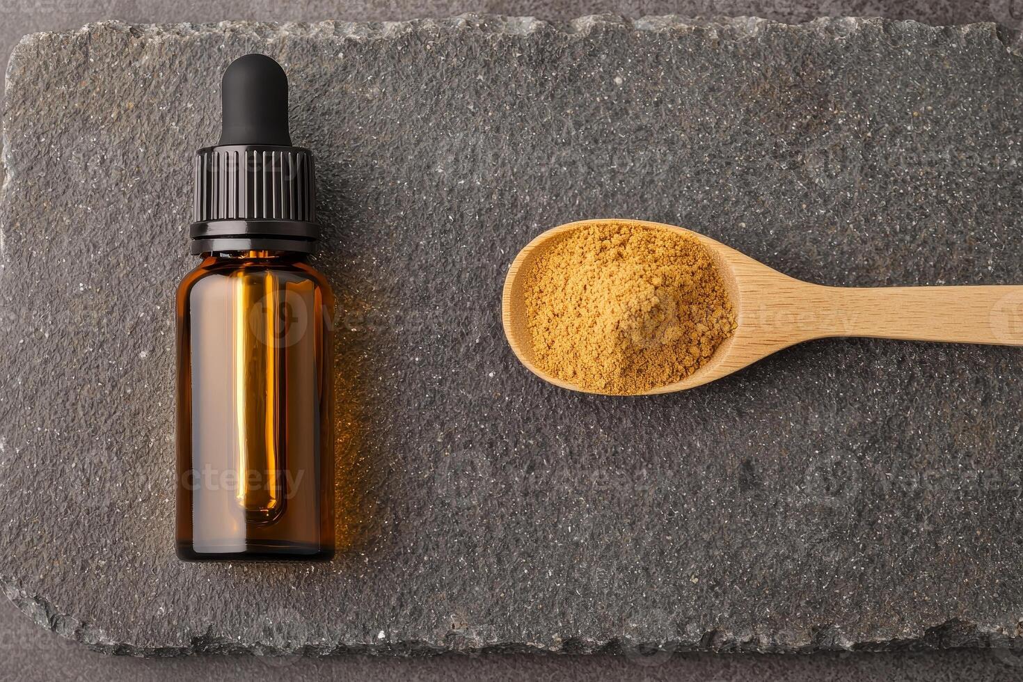 A dropper bottle and a spoonful of powder sit on a textured stone surface, suggesting a focus on natural remedies or essential oils. photo
