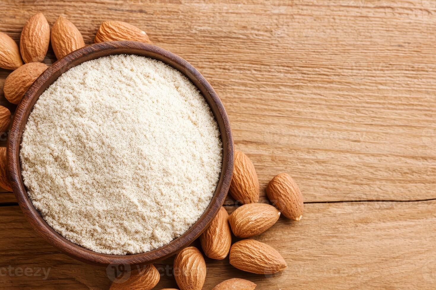 A wooden bowl filled with almond flour surrounded by whole almonds on a rustic wooden surface. photo