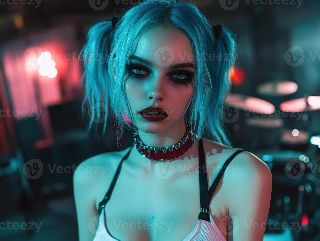 Dark-haired woman with striking makeup and blue hair styled in pigtails, wearing a red spiked choker and a minimal top, standing confidently indoors with a blurred background photo