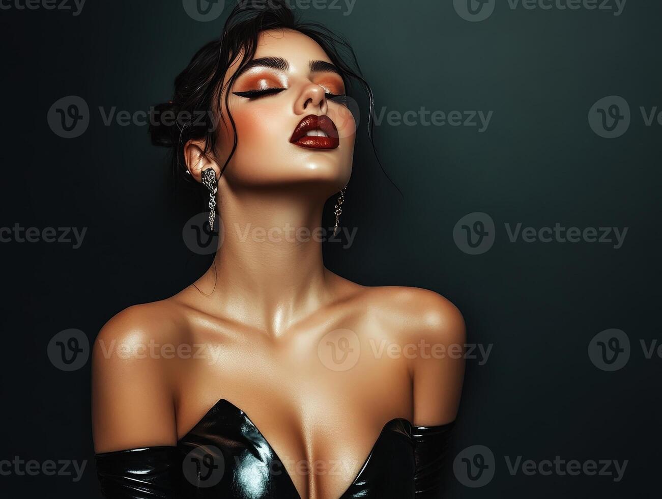 Elegant woman with dark hair in a glossy black strapless dress, wearing sparkling earrings. Her eyes are dramatically lined with eyeliner, and she has bold red lipstick photo
